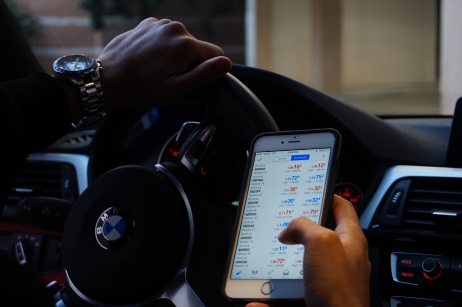 A driver views forex data while behind the wheel, breaching UK law and risking serious distraction on the road.