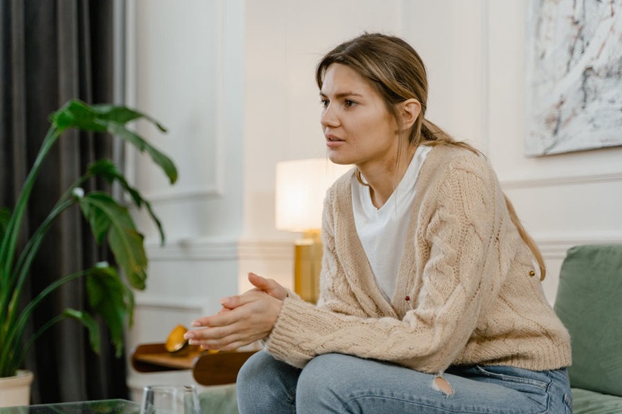 A young woman sits on a sofa, visibly distressed and thoughtful—possibly reflecting on or discussing domestic abuse.