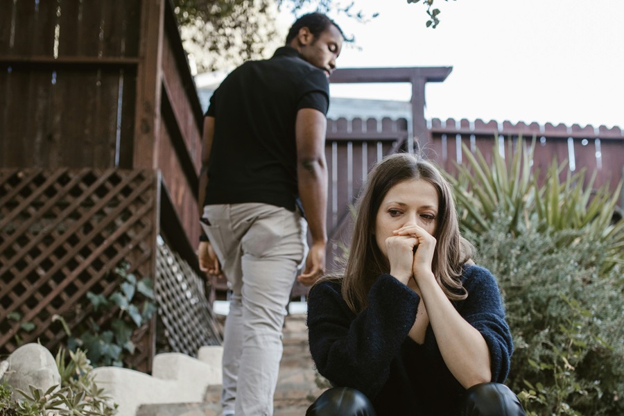 A distressed woman sitting in the foreground while a man walks away from her in a garden, illustrating a difficult separation or divorce