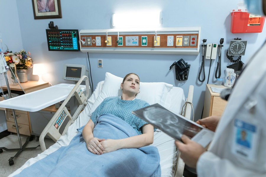 Patient in hospital bed discussing surgical complications with doctor reviewing X-ray
